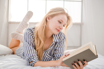 Tender blonde female lying on bed and reading book