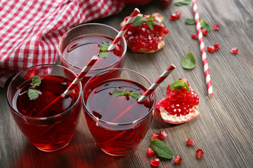 Three glasses of tasty juice and garnet fruit, on wooden background