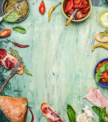 various antipasti with ciabatta bread, pesto and ham on rustic wooden background, top view, frame....
