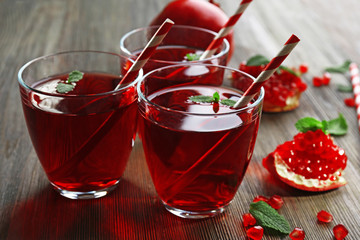 Three glasses of tasty juice and garnet fruit, on wooden background
