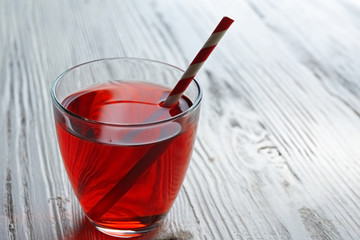 A glass of tasty garnet juice with a straw, on wooden background