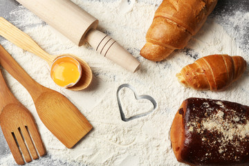 Heart of flour, croissant and  wooden kitchen utensils on gray background
