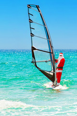 Santa Claus windsurfer go surfing with sailboard at ocean waves