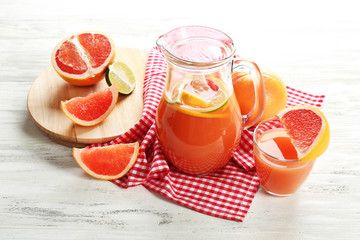 Jar of citrus juice and fresh fruits on light wooden background