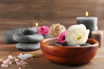 Fototapeta na wymiar Beautiful composition of aroma candle with pebbles and flower in a bowl on wooden background