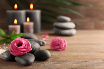 Fototapeta na wymiar Alight wax grey candles with roses and pebbles on wooden background - relax concept