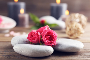 Obraz na płótnie Canvas Alight wax grey candles with roses and pebbles on wooden background - relax concept