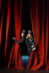 actor and actress in tuxedos open the stage curtain