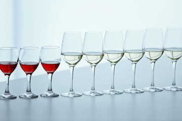 Wineglasses with white, red and pink wine on wooden table on bright background