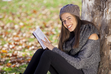 Obraz premium Young girl reading a book lying in the grass on the leaves in the autumn park
