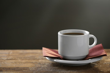 Cup of coffee and coffee grains on wooden table, on gray background