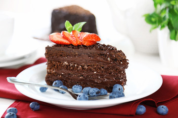 Chocolate cake with chocolate cream and fresh berries on plate, on wooden table, on light background