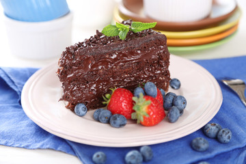 Chocolate cake with chocolate cream and fresh berries on plate, on wooden background