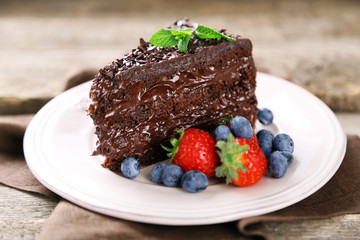 Chocolate cake with chocolate cream and fresh berries on plate, on wooden background