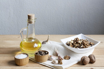 Fototapeta na wymiar Walnuts in a white bowl, garlic, pepper salt and oil on a wooden background, wooden board and white napkin