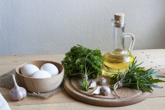 Food ingredients. Oil, eggs, garlic and herbs on wooden table. Wooden board and napkin.