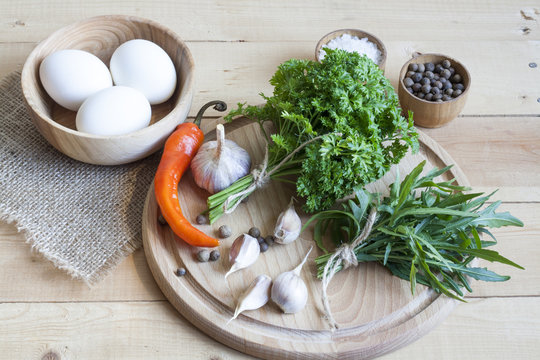 Food ingredients. Eggs, garlic and herbs on wooden table. Wooden board and napkin.