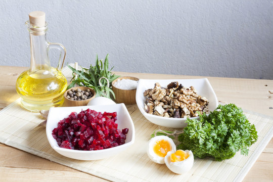 Ingredients for making salad with beets and walnut. The cut products in plates, salt, pepper, herbs, boiled eggs and oil on a wooden table.