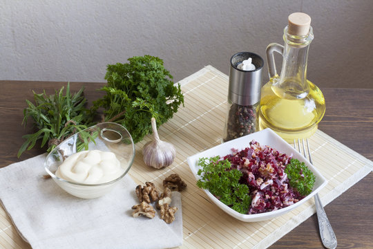 Beetroot salad with walnuts and cream sauce. Nuts, garlic, salt, pepper, herbs, boiled eggs and oil on a wooden table.
