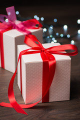 Christmas gift boxes with red bow and lights on wooden surface