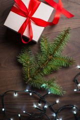 Christmas gift box with red bow and lights on wooden surface