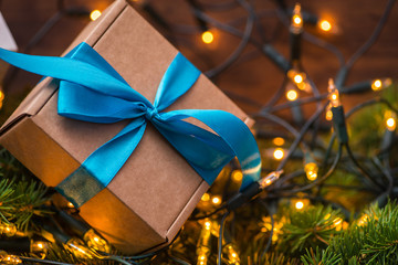 Christmas gift box with blue bow and lights on a fir branch