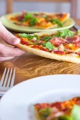 Female hand grabs for a slice of italian style pizza with arugula and prosciutto