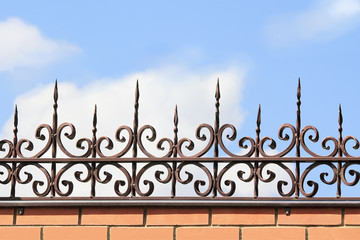 Metal forged fence on a brick wall on the background of sky