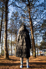 girls wear a black coat standing in a pine forest.