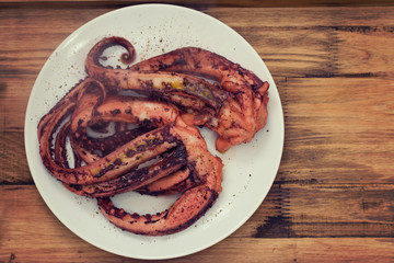 boiled octopus on white plate on brown wooden background