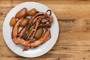 boiled octopus with potato on white plate on brown wooden background