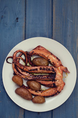 boiled octopus with potato on white plate on blue wooden background
