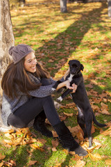 Naklejka na ściany i meble Portrait of a gorgeous brunette woman in the autumn park playing with stray dog. Shallow depth of field