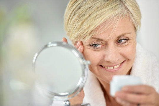 Senior woman in bathroom applying anti-aging lotion