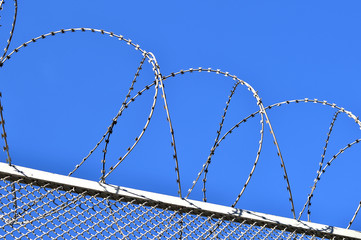 Fence with a barbed wire against the blue sky.