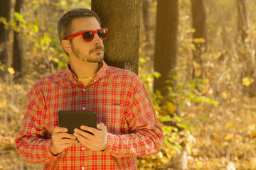 Fototapeta premium Man with a digital tablet leaning against the tree 