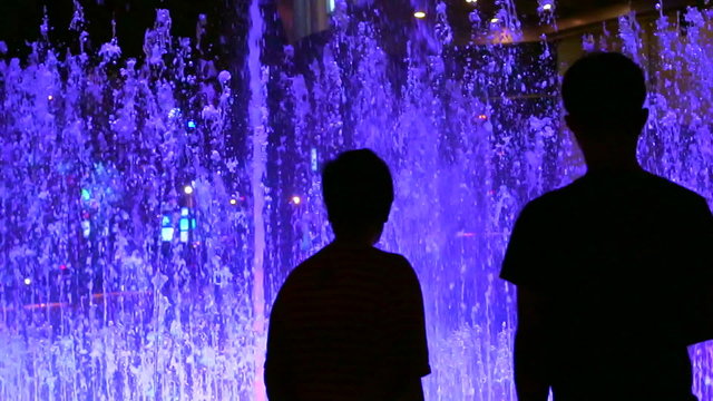 Silhouette of people standing and watching colourful fountain for entertainment