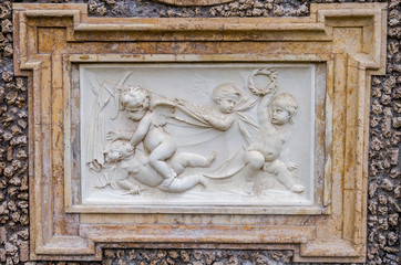 Stone sculpture picture on which two angels fight, and the two look at it in park at Villa Pamphili in Rome, capital of Italy