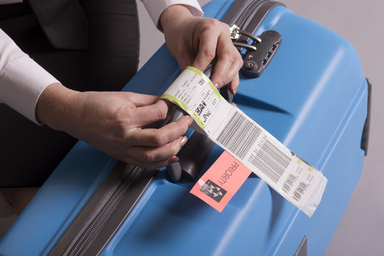 Airline check in luggage tag being attached to a suitcase. Priority tags