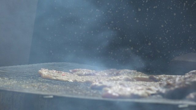 Man grilling pork meat chops on barbecue, flipping pieces with fork, natural light
