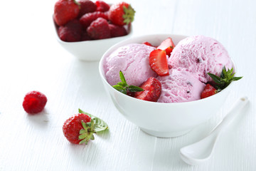 Ice cream in bowl with strawberries on white wooden background