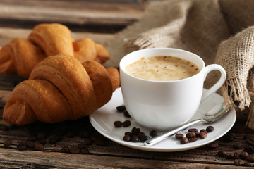 Delicious croissants with cup of coffee on brown wooden backgrou