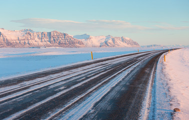 Fototapeta premium The road on a sunny winter day along the snow-capped mountains. The Ring Road (Route 1) of Iceland, between Hof and Jokulsarlon. South of Iceland