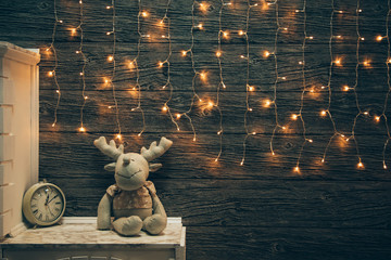 Garland Lights, toy deer, alarm clock on old grunge wooden board. Christmas and New Year decoration.  Christmas lighting on wooden planks 