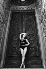 Full-length portrait of a lovely young slim girl in a black bathing suit on a background Gothic building. Portrait of a fashion model.