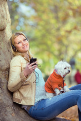 Happy young woman enjoying in a park while listening to music and playing with her dog