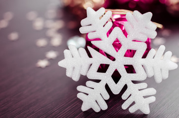 White snowflake on background of magenta and gold xmas baubles with space for text. Merry christmas. Winter holidays. Xmas theme. Happy New Year. Blurred background.