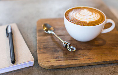 Hot latte art coffee cup on wooden table and note book
