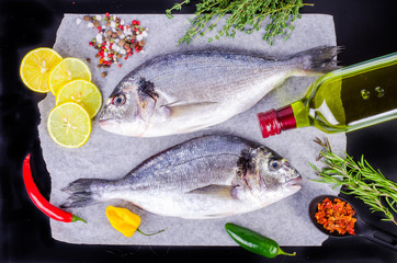 Fresh raw gilthead fishes with lemon, herbs, salt on black background. Healthy food concept. Food frame