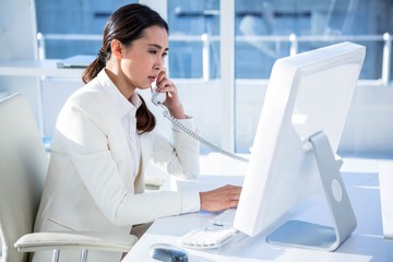 Smiling businesswoman using computer and telephone